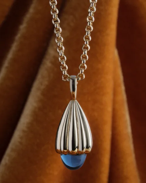 Commercial image of a Casey Perez gold and precious bluestone pendant by photographer Janelle Jones, represented by Pat Bates & Associates, a leading artist rep and photo agency in the luxury commercial and editorial fashion sectors.