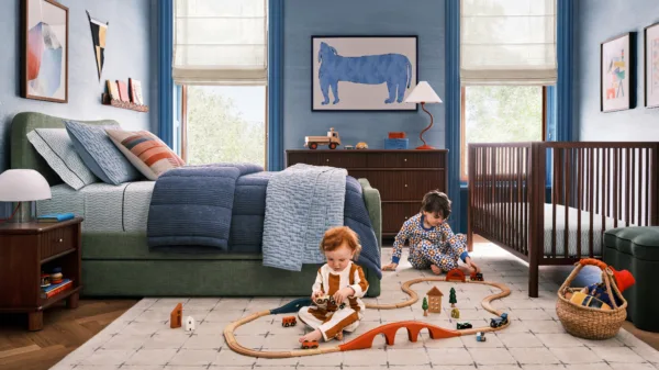 Interior image of a West Elm blue decor bedroom with small children playing with toys next to a cot. Prop styling by Naomi deManana, represented by Pat Bates & Associates, a leading photography agency in the kids brands and advertising sectors.