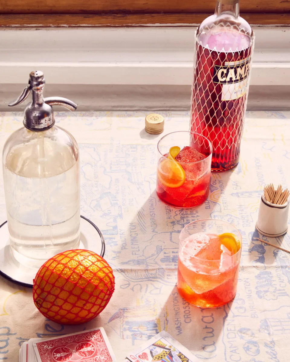 Prop Stylist Oliver Cano and Food and Drink Stylist Liberty Fennell team up to create an intimate gathering, Italian style, with nostalgic summertime vibes. Tabletop with Compari spritz cocktails and a deck of cards on a vintage tablecloth.