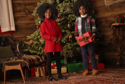 Lifestyle fashion image of kids in front of christmas tree in their christmas outfits for Macy's with makeup by Makeup Artist Paul Fields, represented by Pat Bates & Associates.