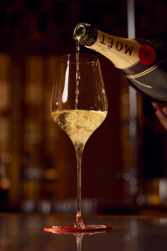 Hospitality Photographer Toby Mitchell for LVMH, photographing details and interiors at two beautiful Moet Chandon champagne bars at Harrods & Royal Albert Hall. Toby expertly captures the iconic brand as sparkling champagne with elegantly reflecting light pours into a stemmed glass with the bar's dark sophistication as a painterly backdrop.